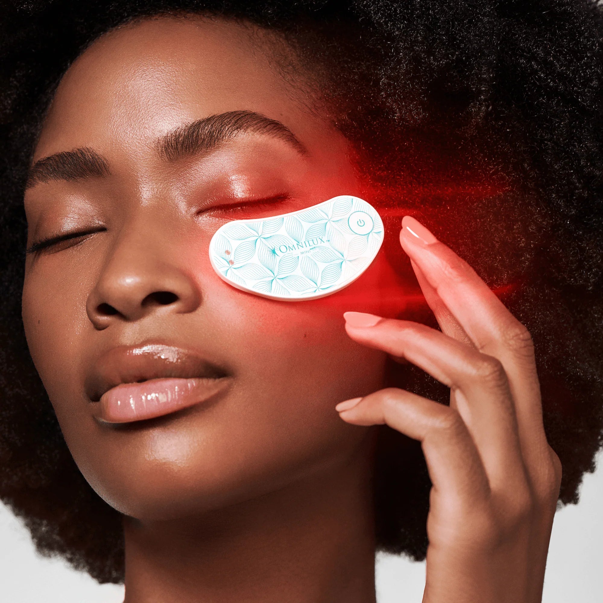 Woman applying an LED eye patch with a red light effect on her face.
